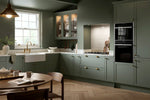 Modern Bella Oakham kitchen with matt smoke green cabinets, a white belfast sink, and a dining table.