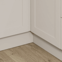 Close-up of a corner with white cabinets and plinth and wooden flooring.