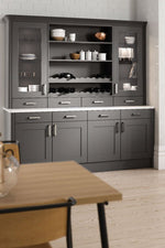 Grey kitchen cabinet with shelves and drawers in a room with wooden floor and white walls.